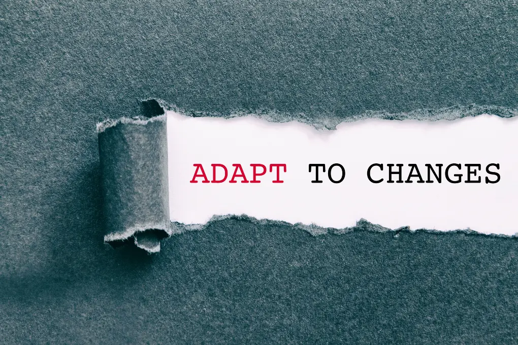 A piece of paper is torn to reveal the words ADAPT TO CHANGES. The word ADAPT is in red, and TO CHANGES is in black