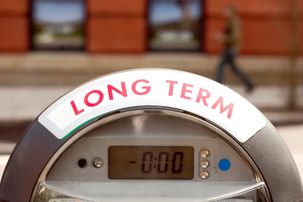 A close-up of a parking meter with a sign that reads LONG TERM in red letters. The meter display shows 0:00